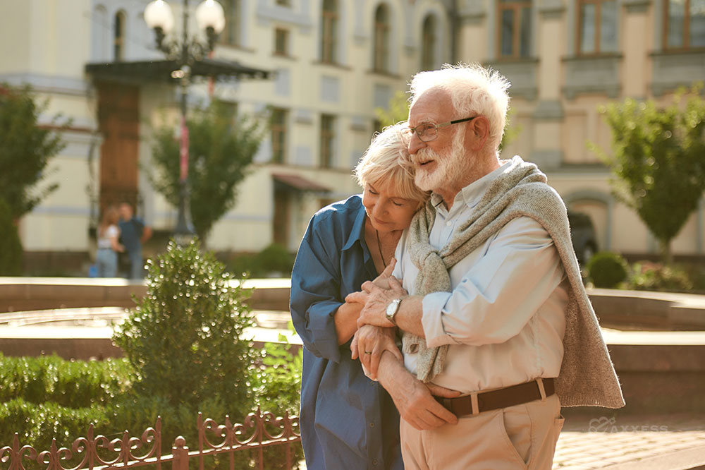 Elderly couple hugs while walking outside at dusk.